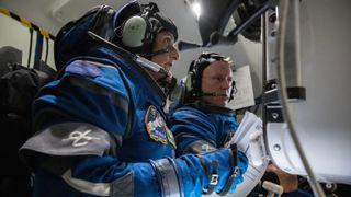 two astronauts training in a simulator with spacesuits and looking at the screen