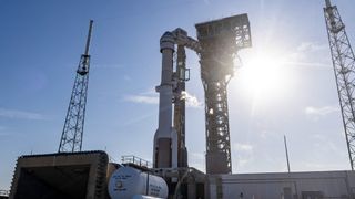 a rocket on a launch pad with the sun behind it and a blue sky surrounded by towers