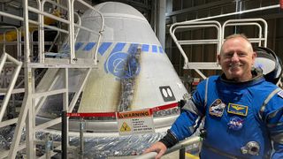 an astronaut in a spacesuit next to a cone-shaped spacecraft in a facility