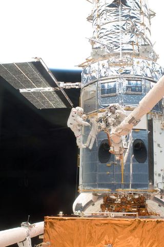 A spaceship with a metal shell is seen close up.  Astronauts serve it.