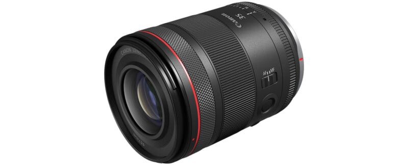 A black Canon RF 35mm f/1.8 IS Macro STM lens is shown on a white background.  The lens features a wide focus ring, a control ring, and an image stabilization switch.  It has a red ring near the front element indicating its L-series status.