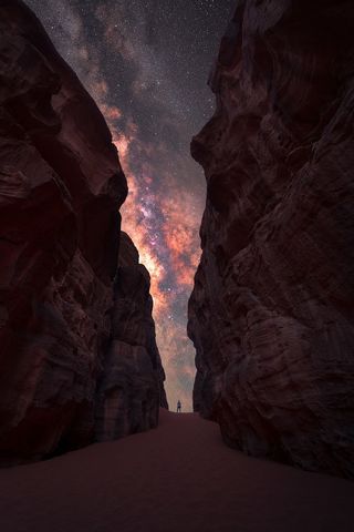 The Milky Way shot between two tall rocks with a lone man standing in the center