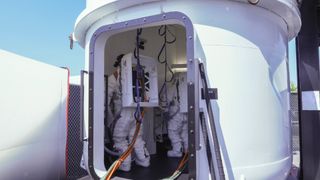 astronauts in white spacesuits stand in a white airlock