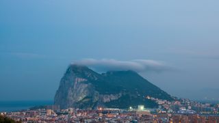 The Rock of Gibraltar at dusk with the Levante Cloud forming above it.  In the foreground is the sprawling border town of La Linea de la Concepción, Cadiz, Spain.