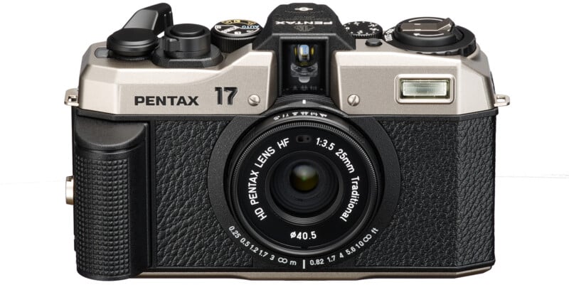 Vintage style Pentax 17 camera with black and silver body.  The camera has a large central lens with a label "HD lens Pentax HF 1:3.5 25mm traditional" and several control dials and buttons on top.  The front features textured grip areas and a built-in flash.