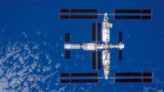 a large T-shaped space station is seen above with Earth below it