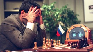 Garry Kasparov holds his head in his hands while sitting on a chessboard