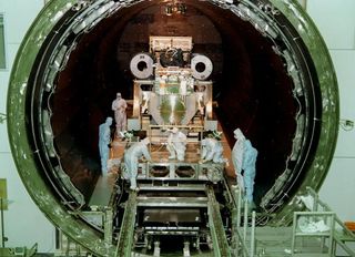 Technicians in clean suits attend a large machine in a round door that spans several meters.