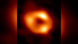 telescope image of a black hole revealed as a fuzzy donut of yellow-orange light surrounding a black center