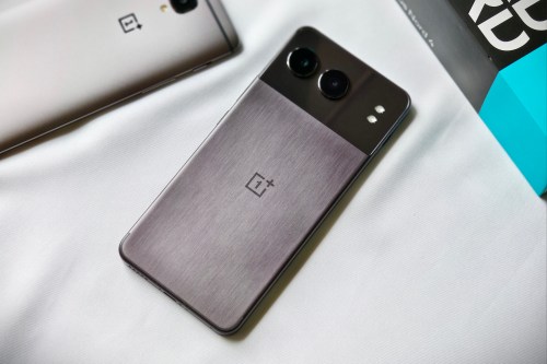 The OnePlus Nord 4 in midnight black with a metallic shell placed over white fabric next to the bronze OnePlus 3T.